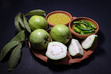 Vibrant arrangement of fresh green guavas (whole and sliced), green chilies, and Kasundi (a popular Bengali spicy mustard sauce) presented in earthen bowls