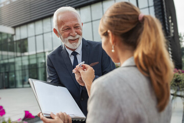 Two business people exchanging knowledge analyzing papers outdoors
