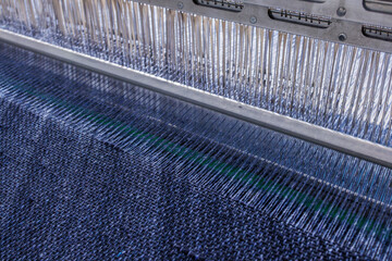 Close-up of modern industrial loom weaving blue textile fabric with tight thread alignment.
