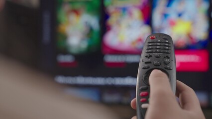 girl controls the TV remote control in room at home, rest on weekend, remote control of a modern smart TV, control TV and movie channels, close-up, blurred display screen, smart page scrolling device.