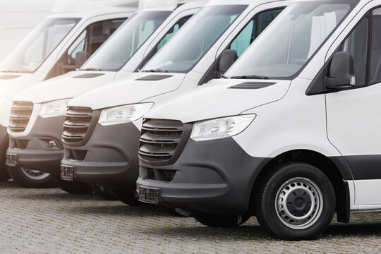 Fleet new modern electric hybrid hydrogen or diesel white vans parked in line row outdoors. Cargo freight industrial courier transportation logistics service. Commercial vehicle maintenance insurance
