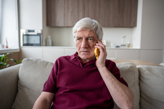 Shock stressed elderly man reacts hanging on phone at home. Scared old male and phone scam danger, fired pensioner, unemployment news, vulnerability, financial stress factors, retiree anxiety