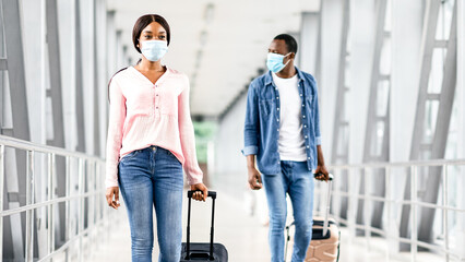 Travelling During Pandemic Concept. Black People In Masks Walking With Luggage At Airport Terminal,...