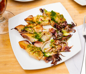 On square white plate are whole squid carcasses,fried on fire.Dish is complemented by glass of cold beer