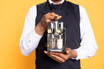Skilled employee with a cruet set greeting clients at luxury restaurant, working in catering industry at a diner. Waiter in uniform presenting condiments and welcoming clients to eat.