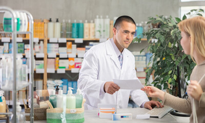 Male pharmacist advises a client on medicines and pills, he has read a medical prescription and...