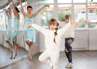 Naklejka premium Boy and girl kids repeat movement while taking hip hop dancing lessons. Female teacher conducts class for students during dance workout and watches performing movements