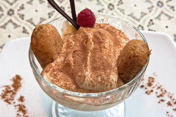 Classic tiramisu in a glass cup elegantly garnished with a raspberry, individual tiramisu dessert