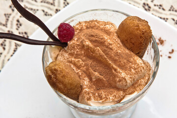 Classic tiramisu in a glass cup elegantly garnished with a raspberry, individual tiramisu dessert