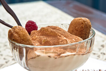 Classic tiramisu in a glass cup elegantly garnished with a raspberry, individual tiramisu dessert