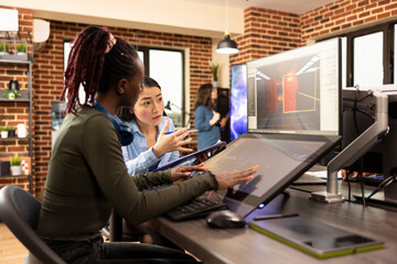 Diverse digital artists working on graphic design and multimedia projects, using a computer and touchscreen monitor. Black and asian women developing creative applications in collaborative workspace.
