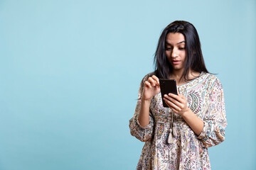 Indian woman happily scrolling on phone to check social media feed, amazed by something. Young...