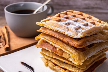 Close-up of a stack of waffles and a cup of coffee behind.