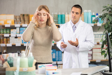 Fototapeta premium Girl visits pharmacy and suffers from headache pain. Customer is looking for affordable remedy to relieve cold symptoms, man pharmacist performing help and consulting