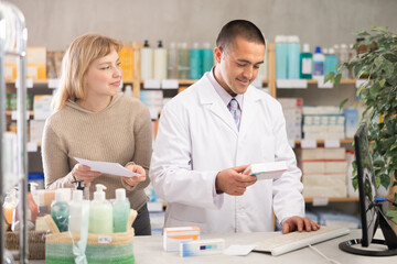 Obraz premium Man pharmacist is working at computer, collaborate with girl client.Electronic database of drugs, international classification of diseases. Detailed list of drugs for treatment of colds.