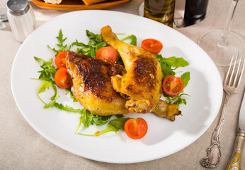 Roasted chicken legs with golden crust served with cherry tomatoes and arugula on plate