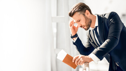 Stressful businessman waiting at airport after flight delays and cancellations, leaning on fence,...