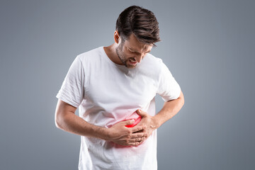Middle-aged man holding his lightened with red right side, suffering from liver pain, grey studio...