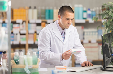 Man in white medical uniform works at computer and makes work notes, enters data into register of...