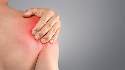 Closeup of topless man suffering from shoulder pain injury, rubbing sore zone over grey studio background, copy space, cropped. Healthcare and medical concept, sports traumatology and orthopedics