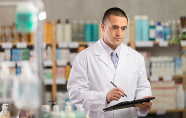 Fototapeta premium Young man pharmacist conducting inventory with tablet in pharmacy