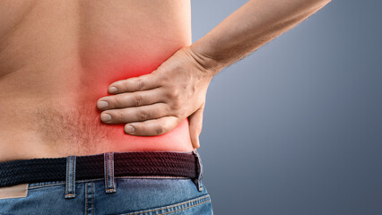 Fototapeta premium Closeup of unrecognizable topless man touching his loin zone highlighted with red, suffering from chronic or acute kidney disease, grey studio background, copy space. Healthcare concept