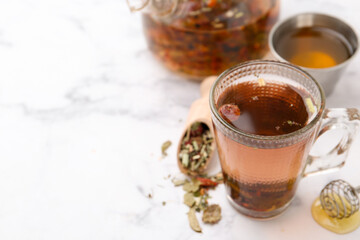 Delicious herbal tea with honey and dry leaves on white marble table. Space for text