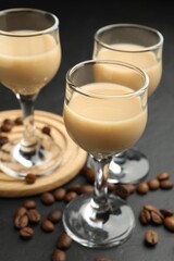 Coffee cream liqueur in glasses and beans on black table, closeup