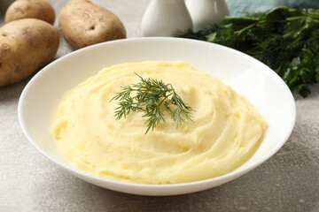 Tasty mashed potato with dill in bowl and raw vegetables on grey textured table, closeup