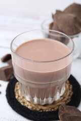 Tasty chocolate milk in glass and pieces of chocolate on white wooden table, closeup
