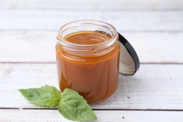 Tasty curry sauce in glass jar and basil on white wooden table, closeup