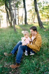 Little girl sits on her dad lap in a clearing in the forest