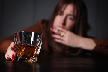 Alcohol addiction. Woman with glass of whiskey smoking cigarette at table indoors, selective focus