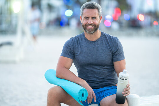 Sport fitness man resting on a bench outdoors. Mature fitness sport model sitting on a bench after a workout. Senior sports man taking a break after fitness. Fit guy resting after fitness.