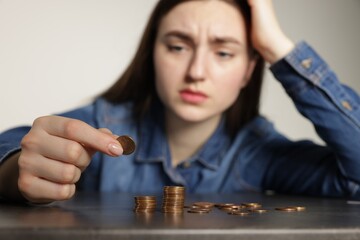 Upset woman counting coins at grey table, selective focus. Financial problems