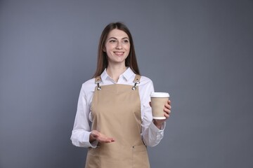 Portrait of smiling barista with paper takeaway cup of hot drink on grey background