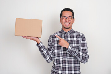 A man smiling happily while pointing at blank cardboard box that he holds