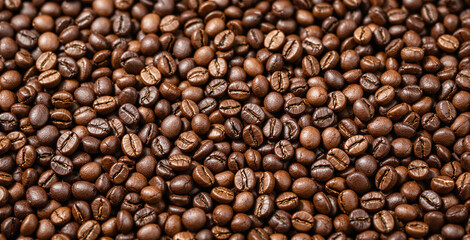 Fototapeta premium Roasted coffee beans fill the entire frame creating a textured food background with detailed surface highlights on a warm neutral backdrop. Ai generative