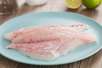 Fresh raw jack fish fillets on blue plate, salt, pepper and limes in the back (Selective Focus, Focus along the middle of the fish) 