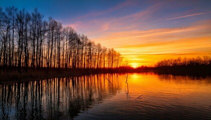 Fototapeta premium Sunset with bare tree forest reflected on water and blazing orange-colored nightfall 