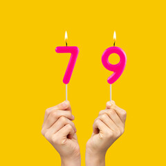 Hands holding birthday candles with number 79 - Yellow background