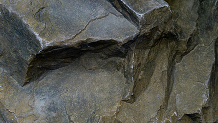 Naklejka premium Close up of a rough textured rock surface. Stone exhibits various shades of gray and brown. With visible cracks and uneven layers suggesting a natural weathered formation.