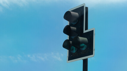 Green traffic lights on the black steel pole. Background of clear blue sky. Signals to pass straight and turn right.