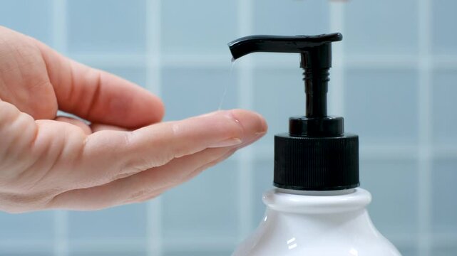 Female hands squeeze soap with dispenser close up against background of blue tiles.