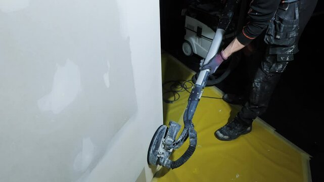 Dust-free sanding process as worker smooths plaster wall on yellow floor cover