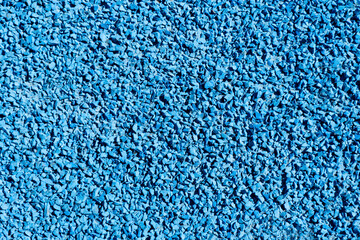 Bright blue granules form the surface of a sports track, offering a colorful and durable area for athletes to practice. Sunlight enhances the vivid color