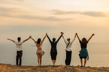 group of people raising their hands together on top of a hill facing the sea