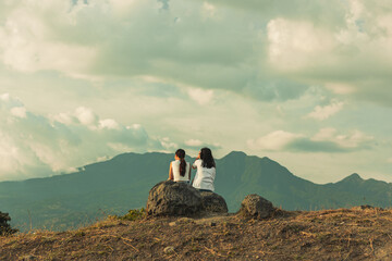two people sitting on a rock, facing the mountain