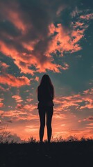 Fototapeta premium Silhouette of woman standing alone against a dramatic sunset sky.