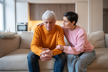 Mature sad depressed couple experiencing hardship as supportive wife comfort hugging distressed husband. Difficulties, financial stress, work issues, strong partnership, overcoming challenges together